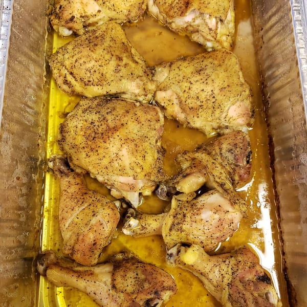 Baked southern chicken pieces, including thighs and drumsticks, in a metal pan with savory juices.