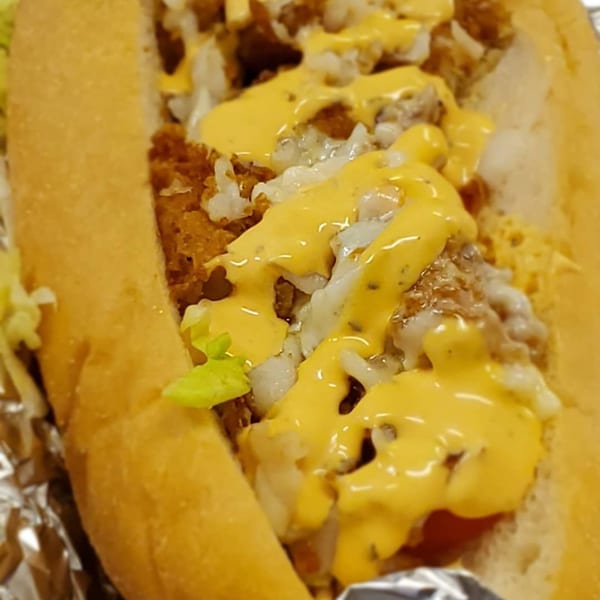 A close-up of a southern soul food po'boy sandwich with fried seafood, cheese, and sauce.
