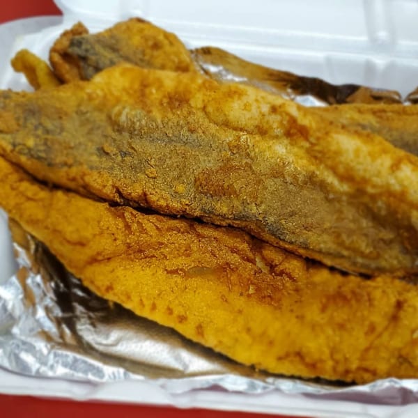 Golden-brown fried fish fillets, seasoned and crispy, served in a white takeout container lined with foil.